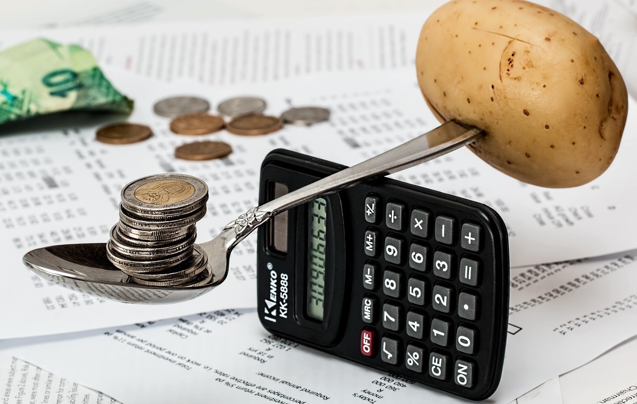 電卓を支点にスプーンにのったコインをジャガイモがあります