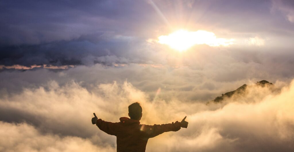 男性が太陽に向かって両手をあげています