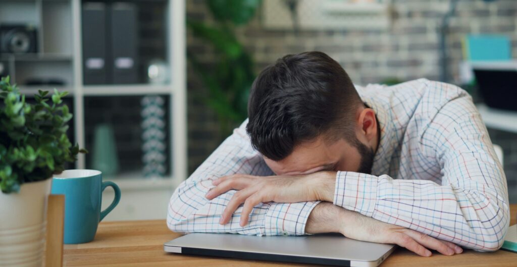 机に顔を伏せて疲れている男性がいます